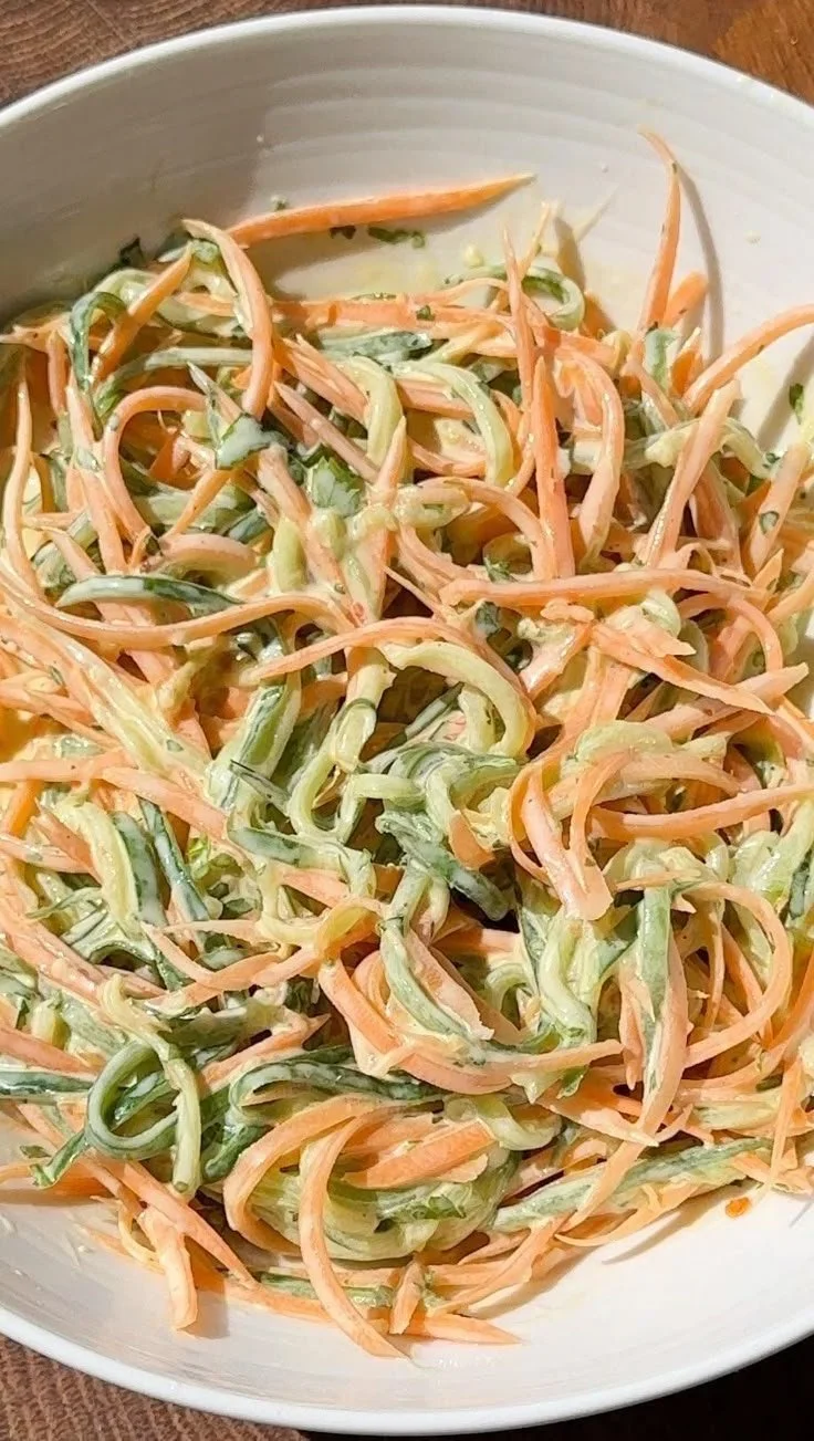 Creamy cucumber and carrot salad in a bowl, garnished with herbs.