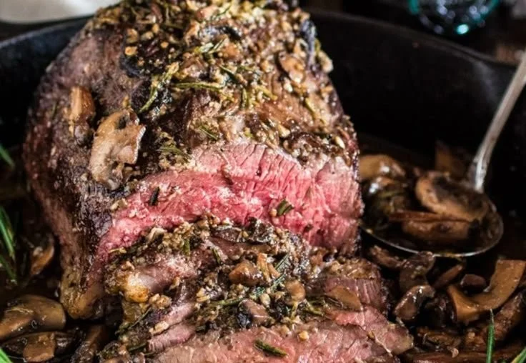 Rosemary and garlic roast beef ready to serve on a wooden cutting board.