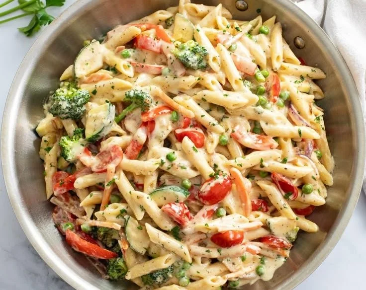 A plate of colorful spring pasta filled with fresh vegetables and herbs.
